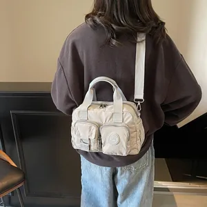 Detail view of a beige nylon crossbody bag with dual handles and multiple zip pockets