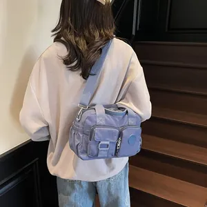Detail of misty blue nylon crossbody bag with multi-pocket design on a wooden staircase