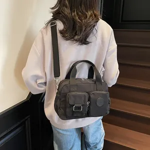 Detail of a black nylon crossbody bag with dual handles and functional front pockets
