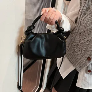 Detail of black pleated handbag featuring knot handle and adjustable shoulder strap