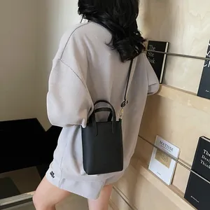 Détail d'un sac seau en cuir noir à motif litchi porté en bandoulière par un mannequin
