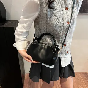 Detail of black pleated crossbody bag with knot handle worn by a model in casual outfit