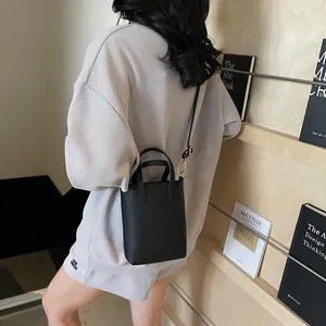 Sac seau noir à motif litchi porté en bandoulière sur une tenue décontractée