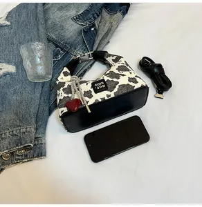 Detail of a chic cow print crescent handbag with heart charm and crossbody strap