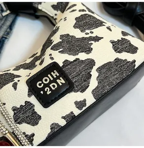Detailed view of cow print shoulder bag featuring rhinestone strap and brand logo patch