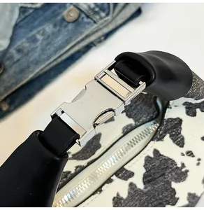 Close-up of cow print shoulder bag with black leather strap and silver metal buckle detail