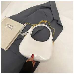 Detail of white glossy crescent bag with gold chain strap on grey blazer background