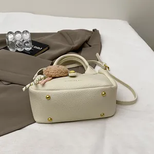 Détails du sac crème texture litchi avec pieds dorés et pendentif décoratif chic
