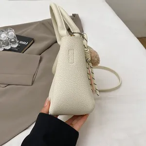 Détails de sac crème à texture litchi avec pompon décoratif et nœud tissé élégant