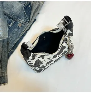Detail of cow print handbag featuring silver buckle and red heart charm on white bedding