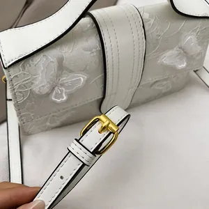 Detail of white lace butterfly embroidery and gold metal buckle on shoulder bag strap