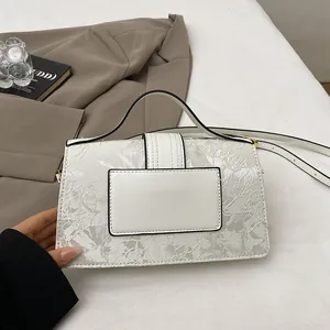 Detail view of white embossed floral textured bag with shoulder strap and handle on props