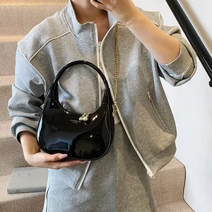 Detail of glossy black patent leather crescent bag with golden chain and metal charm