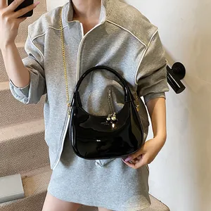 Detail of glossy black hobo bag with gold chain strap on a model in a modern indoor setting