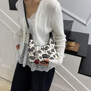 Close-up of stylish cow print crossbody bag featuring a red heart pendant and logo detail