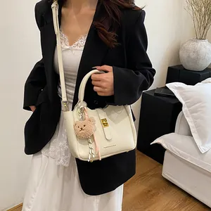 Détail du sac seau crème avec texture litchi, fermoir doré et accessoire d'ours en peluche