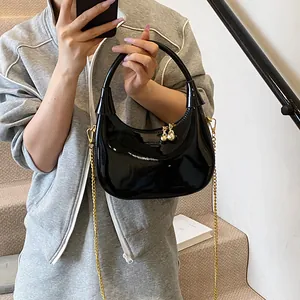 Close-up of glossy crescent bag with gold chain strap and bell pendant on a model