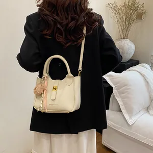 Détail du sac seau blanc cassé avec motif litchi et breloque ours sur un modèle