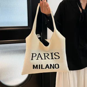 Detail van de gebreide textuur en Paris Milano belettering op de crème witte draagtas