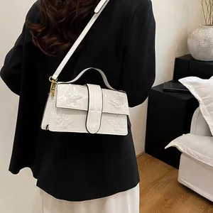 Close-up detail of white square handbag with butterfly embossed pattern and gold hardware