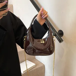 Detail of dark brown glossy crescent bag with gold chain strap and spherical zippers