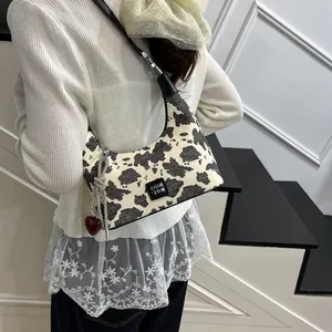 Detail view of cow print hobo bag with red heart charm and silver chain strap