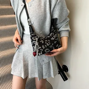 Detailed view of leopard print crescent bag with decorative red heart pendant and silver knot
