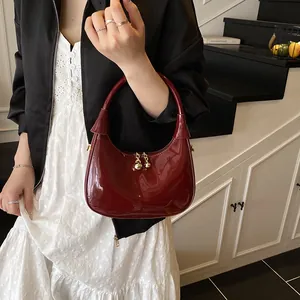 Deep red patent leather crescent bag detail with gold zipper and metallic charm