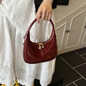 Close-up of a deep red crescent bag with glossy patent finish and gold hardware details