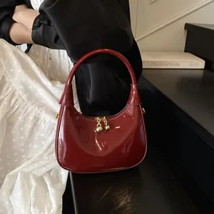 Detail of burgundy crescent bag in glossy patent leather with gold bell-shaped zippers