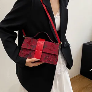 Detailed close-up of red floral lace embroidery and golden hardware on the handbag