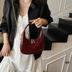 Detail of dark red patent leather crescent bag with golden chain and glossy finish