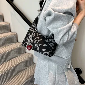 Detail of leopard print crossbody bag with red heart charm and woven strap accents