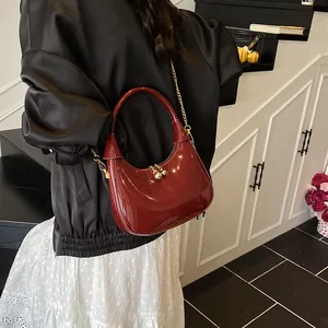 Detail of burgundy glossy crescent bag featuring golden chain and ball zipper pull
