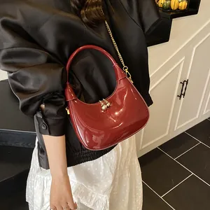 Detail of glossy burgundy crescent bag with polished finish and gold chain strap