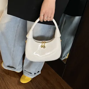 Detail of glossy off-white crescent bag with dual gold spherical zippers and patent leather texture