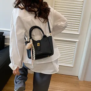 Détail du sac seau noir en cuir avec fermoir doré, pompon et foulard en soie rayé