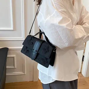 Detail of black crossbody bag with textured butterfly embroidery and top handle grip
