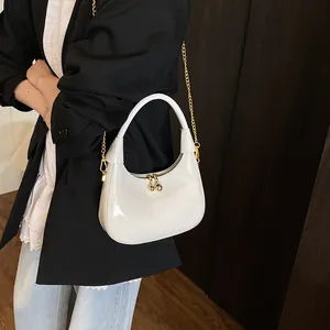 Detailed macro of white glossy crescent bag with golden ball zipper pulls and metal chain