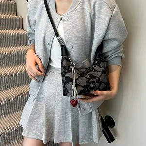 Detail of hobo bag featuring dark textured fabric, metal chain and red heart charm