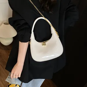 Detail of white glossy crescent bag with gold sphere clasp and elegant chain strap