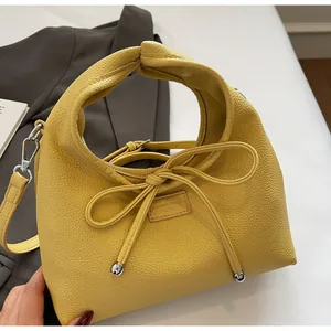 Detail of yellow lychee leather handbag featuring a bow tie and branded fashion label