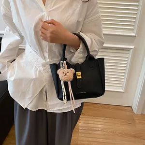 Détail d'un sac seau noir en cuir grainé avec fermoir doré et pendentif ourson