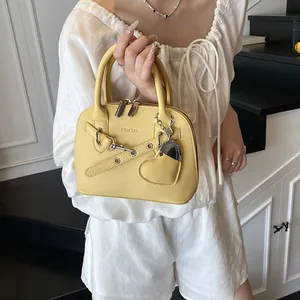 Vue détaillée du sac à main jaune texture litchi avec pendentif cœur argenté et sangles