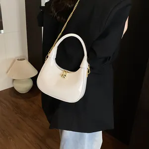 Glossy white crescent hobo bag detail with golden chain strap on a black blazer