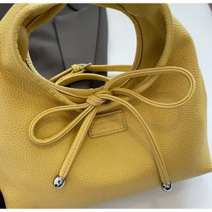 Detail of yellow lychee grain leather handbag featuring a bow and silver metal spheres