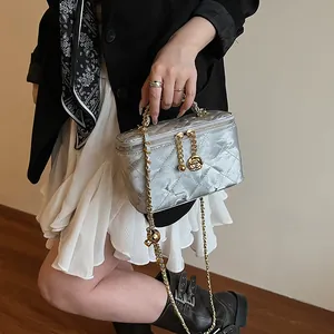 Détail du vanity bag argenté matelassé avec breloque rose dorée et bandoulière chaîne