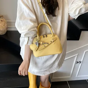 Détail du sac coquille en cuir jaune vif avec pendentif cœur et grain de litchi