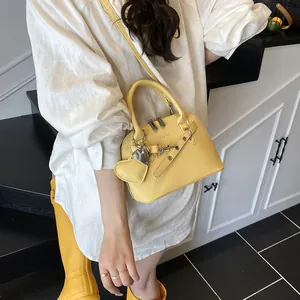 Détail du sac à main jaune en cuir litchi avec breloque cœur porté par un mannequin
