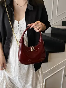 Deep red crescent handbag in glossy patent leather with gold chain strap on model